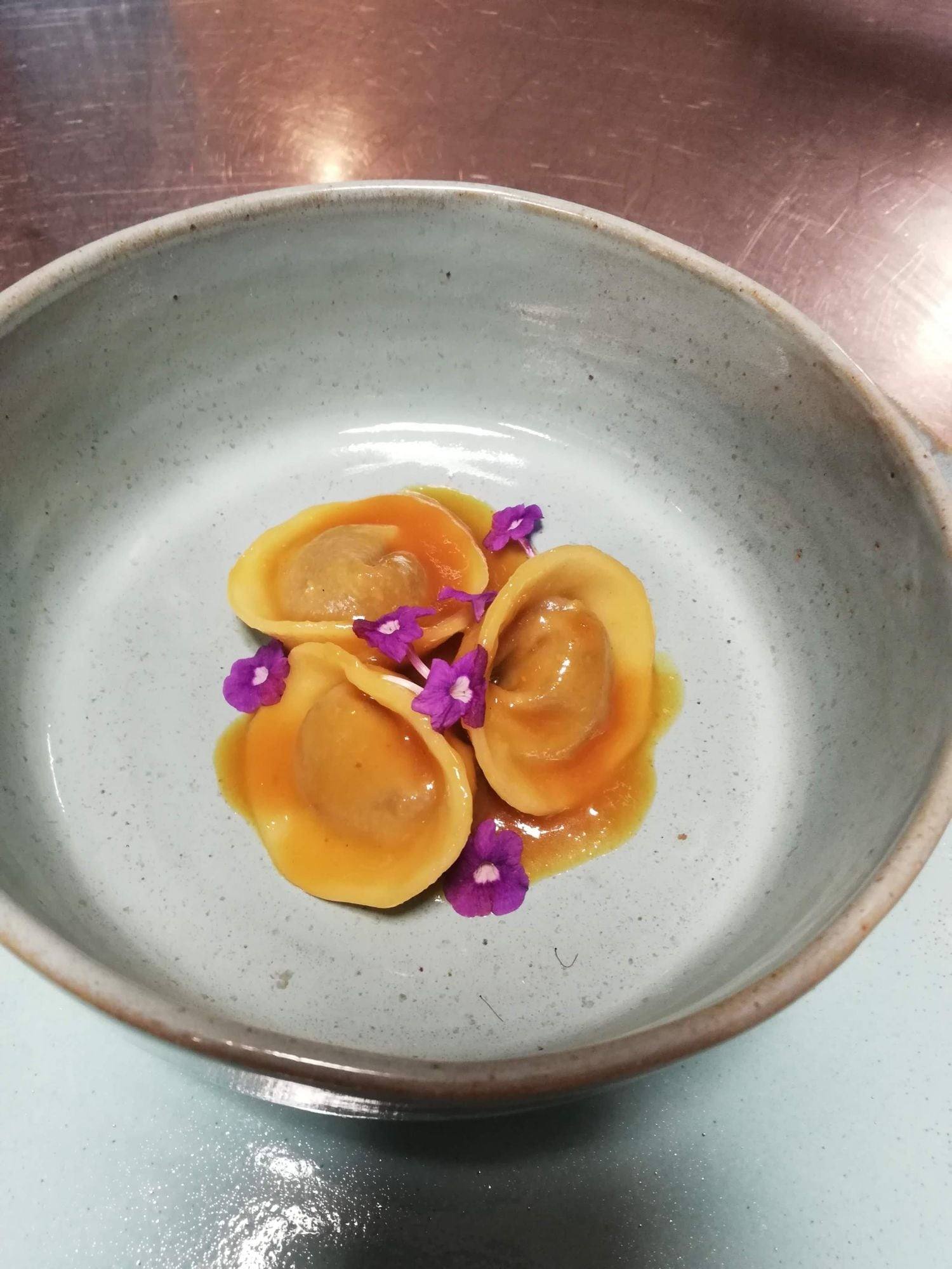 Handmade filled pasta in a golden sauce with edible purple flowers