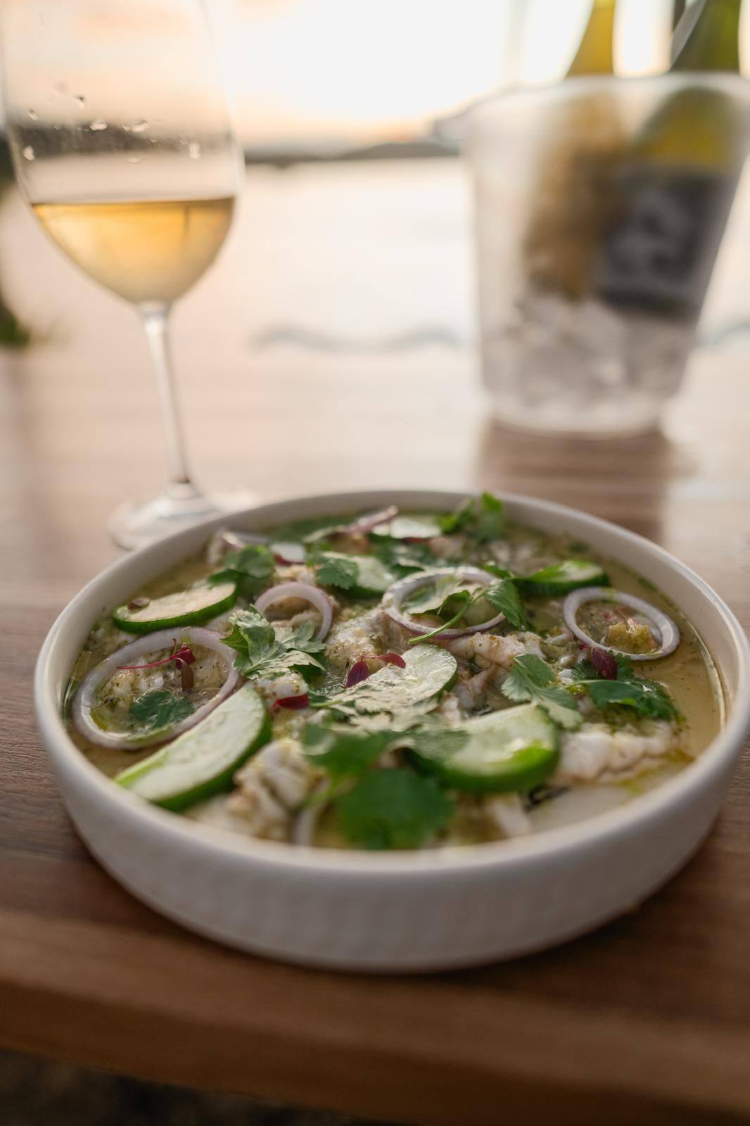 Aguachile with cucumber, red onion and cilantro beside a glass of white wine at sunset